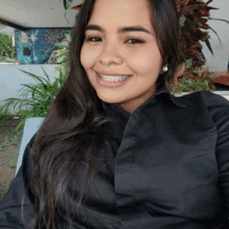 Arley Del Carmen Gómez Ureña smiling at the camera against a tropical background.